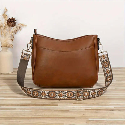 Brown leather handbag with an embroidered strap on a wooden surface.