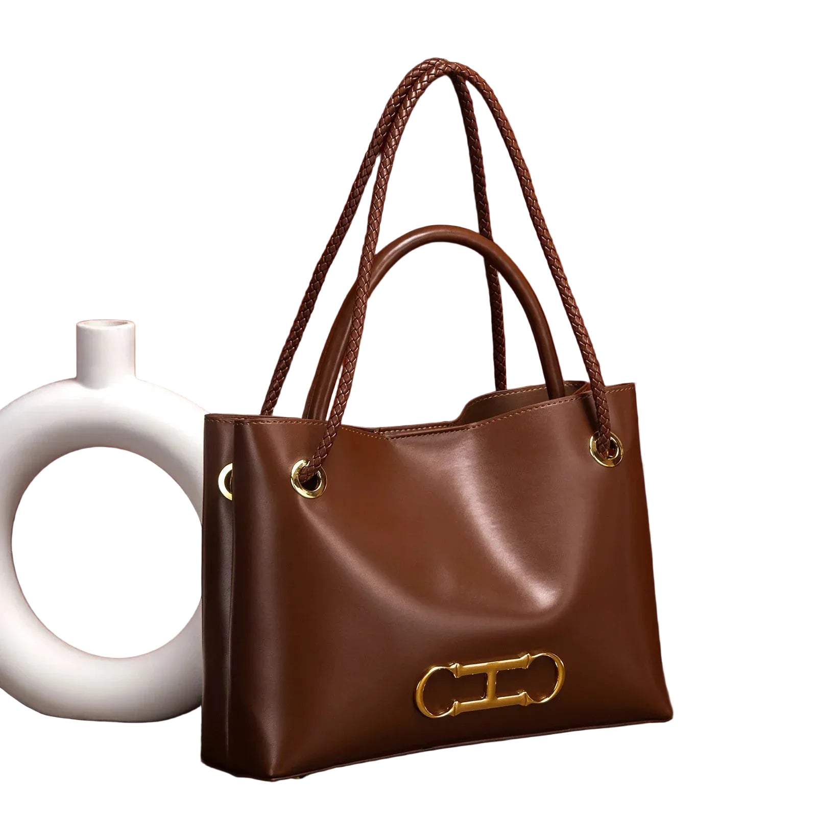 Brown leather handbag with gold accents next to a white vase against a brown curtain background