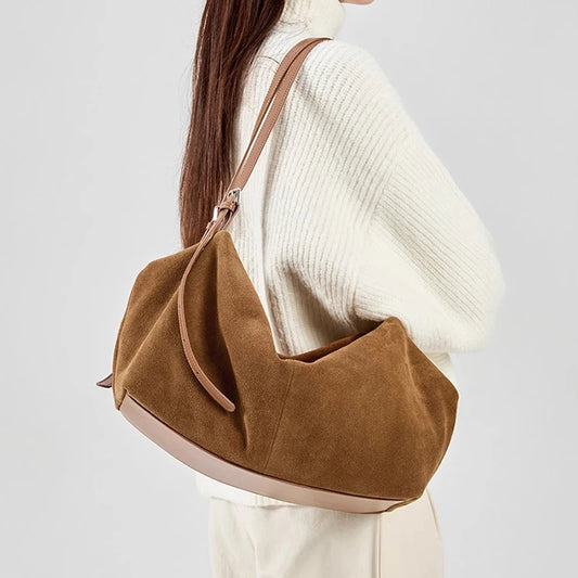 Brown suede handbag worn by a person in a white sweater on a light gray background